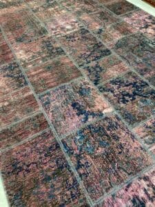 Azerbaijan Tappeti Milano Tappeto patchwork colorato con un mix di toni rosa, blu e scuri. Sono visibili vari motivi rettangolari, che creano un effetto mosaico. Un logo floreale con testo si trova nell'angolo in alto a destra.