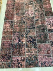 Azerbaijan Tappeti Milano Tappeto patchwork rettangolare con un mix di toni terrosi e un motivo sbiadito e vintage. Un piccolo logo a forma di foglia colorata si trova nell'angolo in alto a destra.