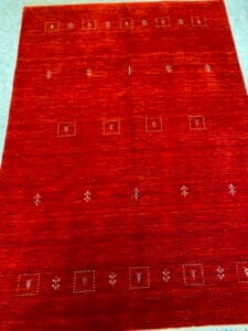 Azerbaijan Tappeti Milano Un tappeto rosso con piccoli motivi geometrici e arborei, caratterizzato da un motivo a foglie multicolori in un angolo.