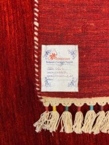 Azerbaijan Tappeti Milano Primo piano di un tappeto rosso con un'etichetta con le istruzioni per la cura e nappe colorate sul bordo.