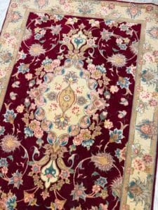Azerbaijan Tappeti Milano Tappeto rettangolare con motivo floreale, caratterizzato da un medaglione centrale beige e sfondo rosso, circondato da fiori colorati e bordi ornati. Una girandola multicolore si trova nell'angolo in alto a destra.