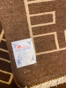 Azerbaijan Tappeti Milano Un tappeto marrone con motivi geometrici, che mostra un'etichetta con la scritta "Azerbaijan" con istruzioni e specifiche per il lavaggio. Un logo colorato è in alto a destra.