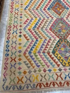 Azerbaijan Tappeti Milano Un tappeto colorato con motivi a zigzag e a rombi in varie tonalità, tra cui rosso, giallo, blu e verde, è esposto su uno sfondo chiaro.