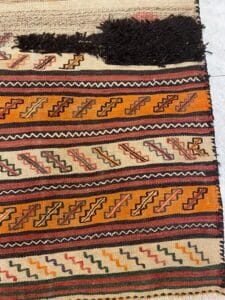 Azerbaijan Tappeti Milano Un tappeto intrecciato con motivi geometrici in rosso, arancione, giallo e verde. Un emblema colorato a forma di fiore è visibile nell'angolo in alto a destra.