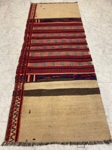 Azerbaijan Tappeti Milano Un tappeto tradizionale intrecciato con motivi geometrici in rosso e beige, adagiato su un pavimento piastrellato chiaro.