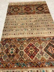 Azerbaijan Tappeti Milano Un tappeto colorato con motivi geometrici e floreali è esposto su un pavimento piastrellato chiaro.