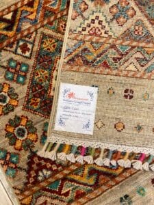 Azerbaijan Tappeti Milano Tappeti colorati intrecciati con intricati motivi geometrici, tra cui un'etichetta con la scritta "Tappeto persiano o azero" e un piccolo logo colorato nell'angolo in alto a destra.