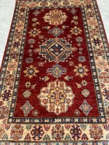 Azerbaijan Tappeti Milano Su un pavimento piastrellato è adagiato un tappeto riccamente decorato con disegni geometrici e motivi floreali nei toni del rosso, del crema e del blu.