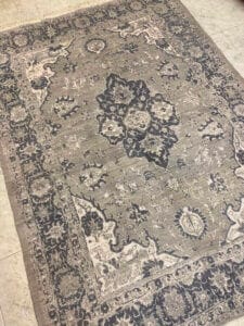 Azerbaijan Tappeti Milano Su un pavimento piastrellato è appoggiato un tappeto rettangolare decorato con un motivo floreale grigio e blu scuro.