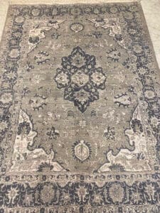 Azerbaijan Tappeti Milano Tappeto ornato in stile persiano con motivi intricati in tonalità di grigio, nero e bianco. Un logo colorato è esposto nell'angolo.