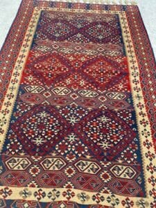 Azerbaijan Tappeti Milano Tappeto con motivi colorati e motivi geometrici nei toni del rosso, blu e beige, con una piccola farfalla nell'angolo in alto a destra.