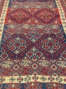 Azerbaijan Tappeti Milano Tappeto persiano con intricati motivi geometrici rossi, blu e bianchi, caratterizzati da triangoli e rombi.