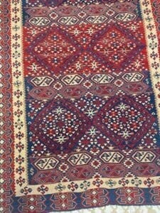 Azerbaijan Tappeti Milano Tappeto con motivi geometrici rossi, blu e beige e una farfalla appoggiata sull'angolo.