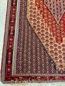 Azerbaijan Tappeti Milano Primo piano di un tappeto intrecciato multicolore con intricati motivi geometrici e un piccolo logo colorato nell'angolo in alto a destra.