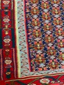 Azerbaijan Tappeti Milano Primo piano di un tessuto intrecciato colorato e dettagliato, con intricati motivi geometrici e disegni nelle tonalità del rosso, del blu e del verde.