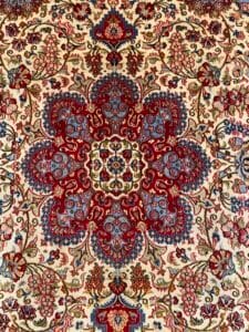 Azerbaijan Tappeti Milano Tappeto persiano floreale ornato con intricati motivi rossi, blu e beige. Un logo a forma di stella multicolore è presente nell'angolo in alto a destra.