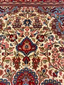 Azerbaijan Tappeti Milano Intricato tappeto persiano con motivi floreali e geometrici in rosso, blu e crema. Un logo a forma di stella colorata è nell'angolo in alto a destra.