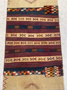 Azerbaijan Tappeti Milano Un tappeto intrecciato colorato con motivi geometrici e strisce. Il design include rossi, blu e arancioni vivaci su uno sfondo chiaro. Motivo a scacchi parziale visibile in un angolo.