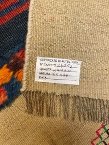 Azerbaijan Tappeti Milano Primo piano di un'etichetta su un arazzo intrecciato, che mostra dettagli di autenticità e motivi colorati lungo i bordi.