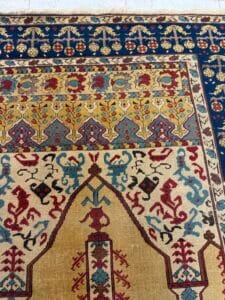 Azerbaijan Tappeti Milano Primo piano di un tappeto persiano ornato e colorato con intricati motivi floreali e geometrici nei toni del blu, rosso, giallo, crema e beige. Nell'angolo in alto a destra è presente il logo di una foglia multicolore.