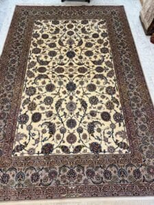 Azerbaijan Tappeti Milano Tappeto rettangolare in stile persiano con un intricato motivo floreale in colori scuri su sfondo crema, circondato da un bordo ornato. Il logo di una foglia colorata si trova nell'angolo in alto a destra dell'immagine.