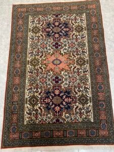 Azerbaijan Tappeti Milano Un tappeto persiano multicolore con intricati motivi geometrici e floreali è adagiato su un pavimento piastrellato.