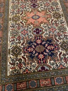 Azerbaijan Tappeti Milano Tappeto con motivi intricati, disegni geometrici e motivi floreali nei colori della terra, con un piccolo disegno di una sedia e foglie in un angolo.