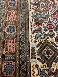 Azerbaijan Tappeti Milano Tappeto con motivo geometrico caratterizzato da file di forme e motivi multicolori in toni terrosi. Un ricamo colorato a forma di farfalla è visibile sul lato destro.