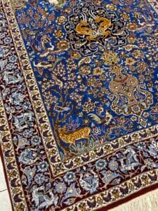Azerbaijan Tappeti Milano Un tappeto in stile persiano blu e oro, decorato con intricati motivi floreali e animali e con un logo geometrico colorato in un angolo.