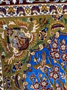 Azerbaijan Tappeti Milano Intricati motivi floreali e di foglie su un tappeto colorato e ornato con sezioni blu, verdi e bordeaux, caratterizzato da un motivo a farfalla in un angolo.