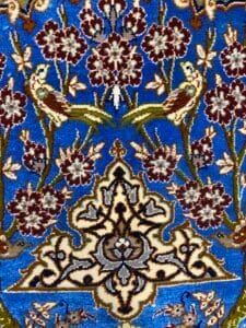 Azerbaijan Tappeti Milano Un arazzo blu dettagliato presenta motivi floreali, due uccelli e intricati disegni geometrici in rosso, verde e crema.