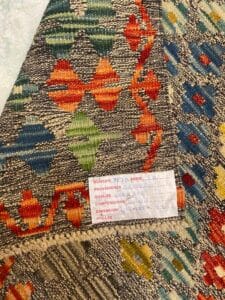 Azerbaijan Tappeti Milano Primo piano di un tessuto intrecciato colorato con motivi geometrici. Un'etichetta con dettagli scritti a mano sull'articolo è cucita sul tessuto.