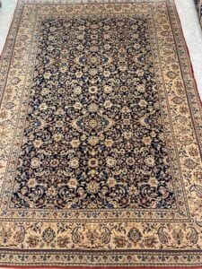 Azerbaijan Tappeti Milano Tappeto decorato in stile persiano con intricati motivi floreali blu e beige bordati da dettagliati disegni geometrici, esposto su un pavimento piastrellato.