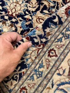 Azerbaijan Tappeti Milano Angolo di un tappeto decorato a mano con intricati disegni floreali nei toni del blu, crema e rosso.