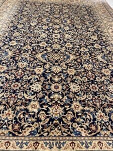 Azerbaijan Tappeti Milano Tappeto ornato in stile persiano con motivi floreali e di vite simmetrici in beige e blu navy. Un logo colorato a forma di mulino a vento è posizionato nell'angolo in alto a destra.