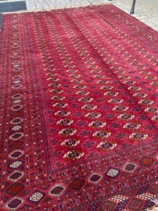 Azerbaijan Tappeti Milano Un grande tappeto rosso in stile persiano, decorato con intricati motivi geometrici e floreali, è steso all'aperto su un pavimento in pietra.