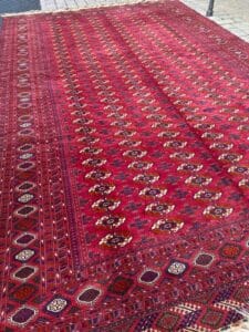 Azerbaijan Tappeti Milano Un grande tappeto rosso decorato con intricati disegni geometrici è esposto all'aperto, su una superficie piastrellata.