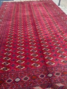 Azerbaijan Tappeti Milano Un tappeto rosso con motivi geometrici e floreali ripetuti, steso su un pavimento in pietra.