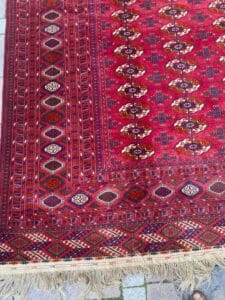 Azerbaijan Tappeti Milano Tappeto rosso con motivi geometrici e bordo sfrangiato, che ricopre parzialmente piastrelle in pietra chiara.