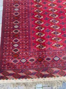 Azerbaijan Tappeti Milano Un tradizionale tappeto rosso con intricati disegni geometrici e bordi sfrangiati, mostrato parzialmente.