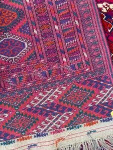 Azerbaijan Tappeti Milano Primo piano di un tappeto colorato, intrecciato con motivi geometrici in rosso, viola, blu e bianco.