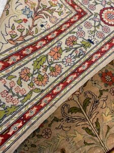 Azerbaijan Tappeti Milano Due tappeti sovrapposti con motivi floreali nei toni del beige, rosso e verde; nell'angolo in alto a destra si trova una piccola farfalla colorata.