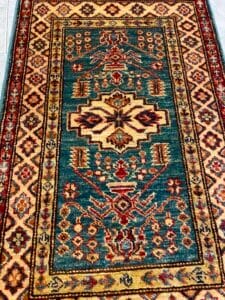 Azerbaijan Tappeti Milano Un tappeto orientale decorato con disegni geometrici e un logo a forma di foglia colorata nell'angolo in alto a destra.