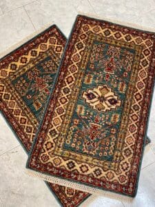 Azerbaijan Tappeti Milano Due tappeti rettangolari con motivi intricati, raffiguranti disegni blu, rossi e beige, posizionati su un pavimento piastrellato.