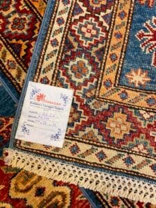Azerbaijan Tappeti Milano Un tappeto con motivi colorati, un'etichetta con dettagli scritti a mano e un bordo decorativo con frange.