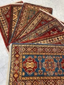 Azerbaijan Tappeti Milano Diversi tappeti orientali colorati e decorati sono disposti a ventaglio su un pavimento piastrellato chiaro.