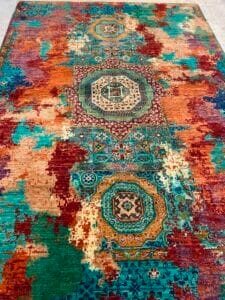 Azerbaijan Tappeti Milano Colorato tappeto intrecciato con motivi geometrici in blu, verde acqua e rosso, con un design astratto e anticato e un logo decorativo nell'angolo in alto a destra.