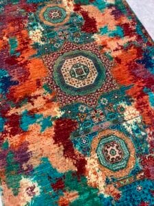 Azerbaijan Tappeti Milano Un tappeto colorato con motivi geometrici a medaglioni nei toni del blu, arancione, rosso e verde acqua, caratterizzato da un design astratto e anticato.