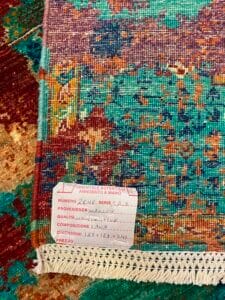 Azerbaijan Tappeti Milano Primo piano di un colorato tappeto intrecciato con un'etichetta che riporta dettagli quali origine, qualità, composizione, dimensioni e un logo nell'angolo in alto a destra.