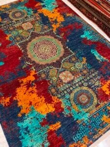 Azerbaijan Tappeti Milano Un tappeto rettangolare caratterizzato da intricati motivi geometrici al centro e da un design anticato nei toni del rosso, blu, arancione e turchese.